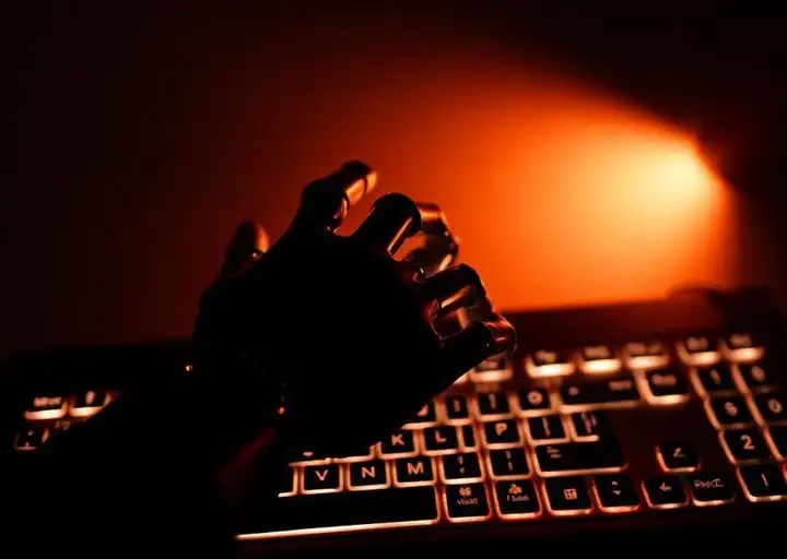 Shadow of a robot hand over a glowing keyboard in high-contrast noir light